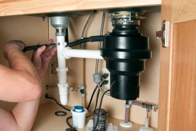 Plumber repairing a garbage disposal beneath a kitchen sink in Indio