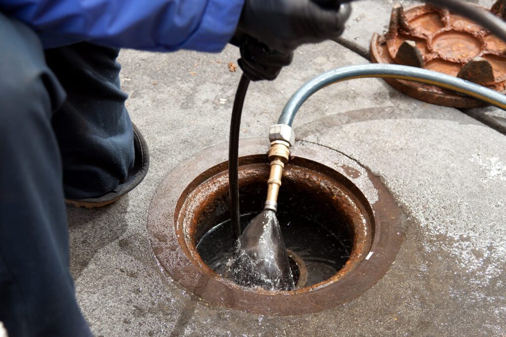 Plumber hydro jetting a sewer line through a manhole in Indio